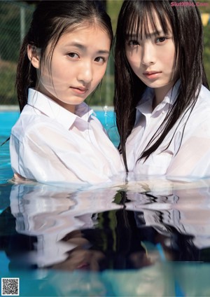 Two young women sitting on the floor in front of a window.