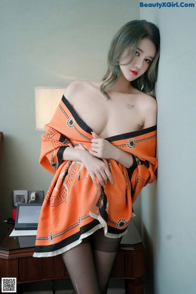 A woman in an orange and black dress leaning against a wall.
