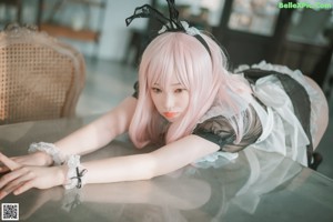 A woman with long pink hair sitting on a bed.