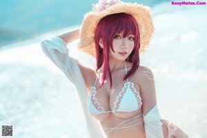 A woman in a bikini and a straw hat on the beach.