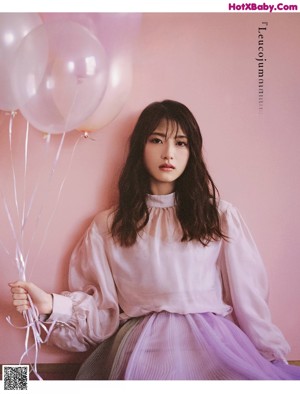 A woman sitting on the floor holding a bunch of balloons.