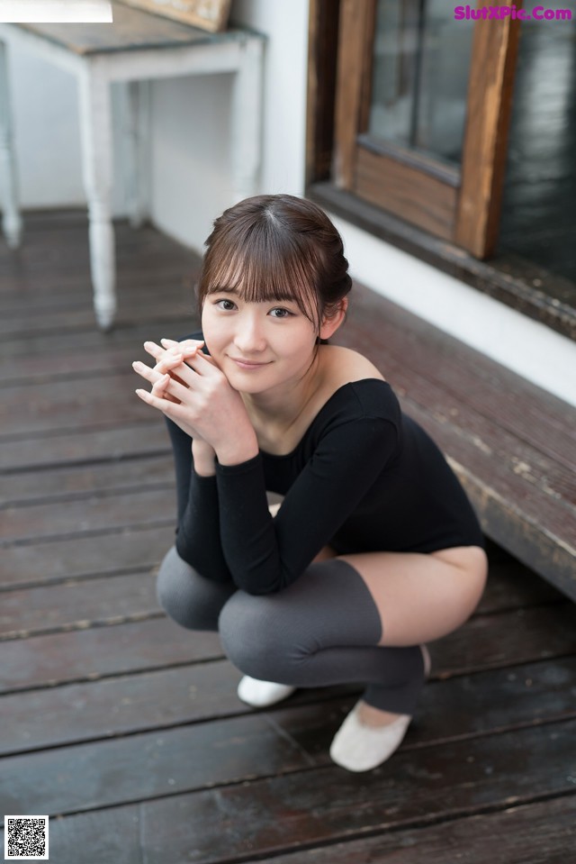 A woman sitting on a wooden floor with her hands clasped together.