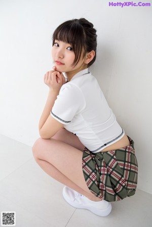 A woman in a white shirt and plaid skirt leaning against a wall.
