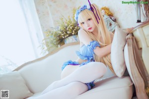 A woman in a blue dress and white stockings laying on a couch.