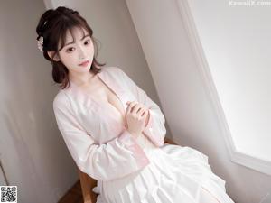 A woman in a yellow and white dress sitting on a bed.