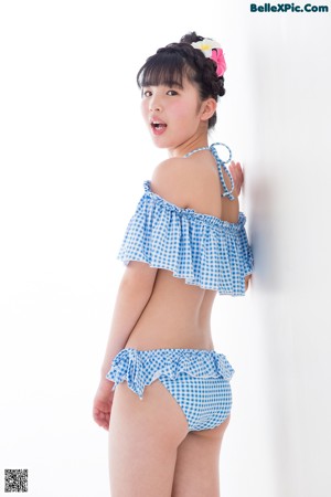A young girl in a blue and white gingham bikini standing on a scale.