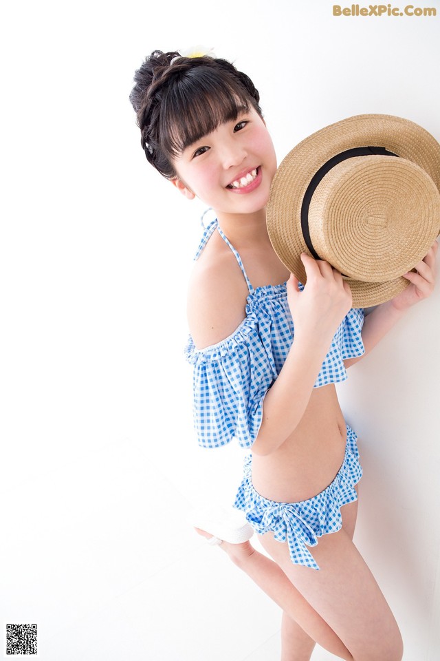 A young girl in a blue and white bikini holding a straw hat.