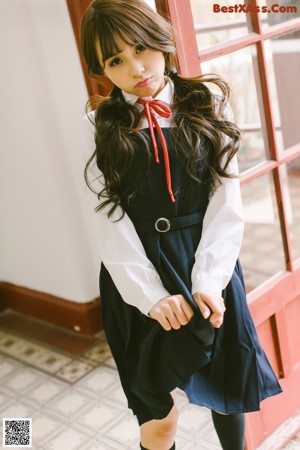 A young girl in a blue and white dress leaning against a door.