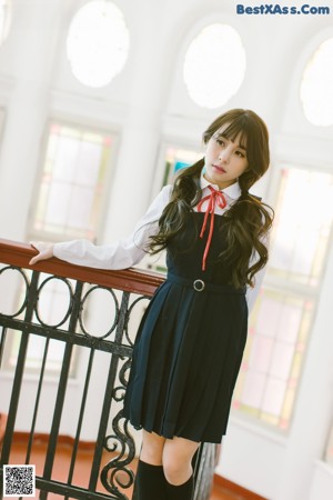 A woman in a school uniform leaning against a fence.