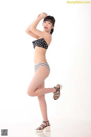 A woman in a black and white bikini leaning against a wall.