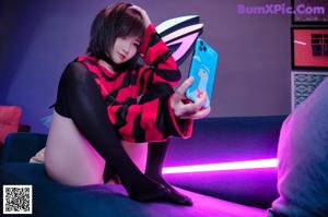 A woman in a black and red striped shirt is sitting on a bed.