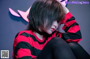 A woman in a red and black striped shirt is posing on a bed.