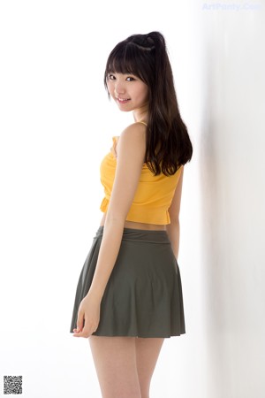 A woman in a yellow top and green skirt posing for a picture.